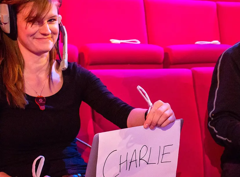 Michelle Reeve holding up a sign that says 'Charlie' next to a cameraman who looks intently at something off camera