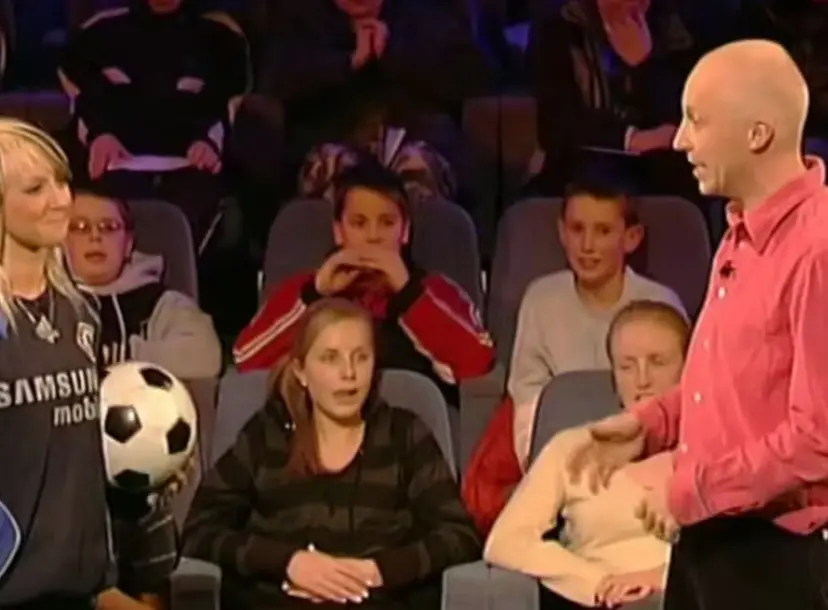 Marcus du Sautoy standing with a teenage girl who is holding a football, in front of an audience 