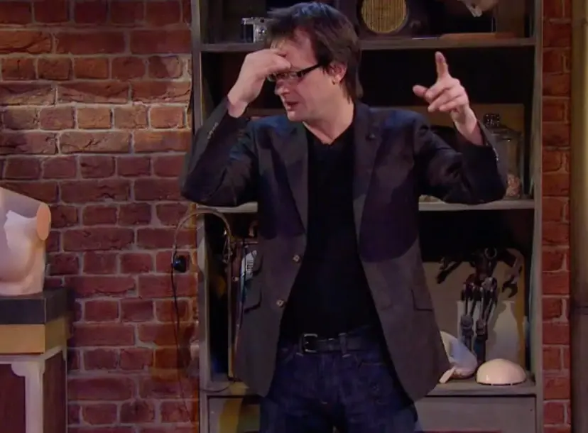 Bruce Hood with one hand on his head, standing in front of a bookcase 