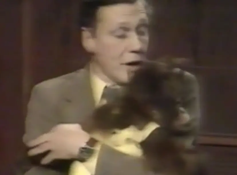 David Attenborough holding a monkey, who is wearing a yellow dungarees