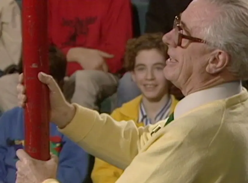 Charles Taylor holding a large red metal rod, with children smiling in th ebackground of the Ri theatre