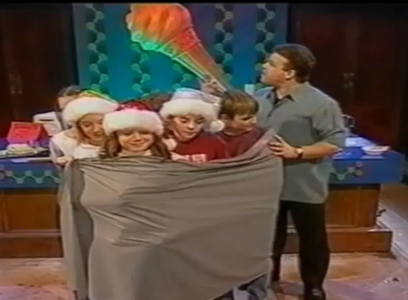 Tony Ryan stands next to a group of children who are standing together, wrapped in a sheet