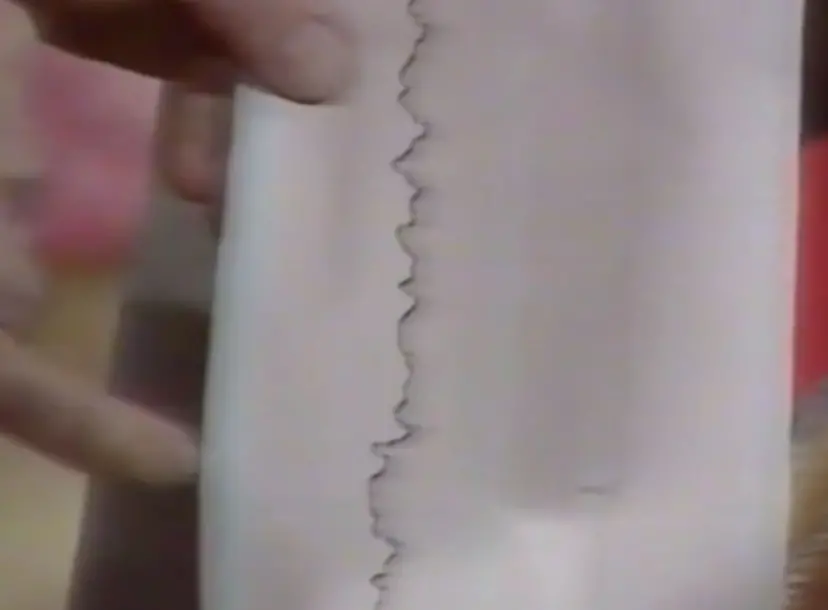 a hand pointing at a piece of paper that has a vertical wobbly line 