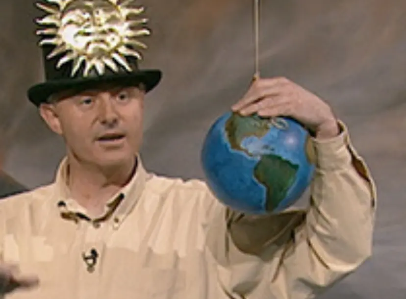 James Jackson wearing a top hat with a sun stitched onto it, holding a small earth globe