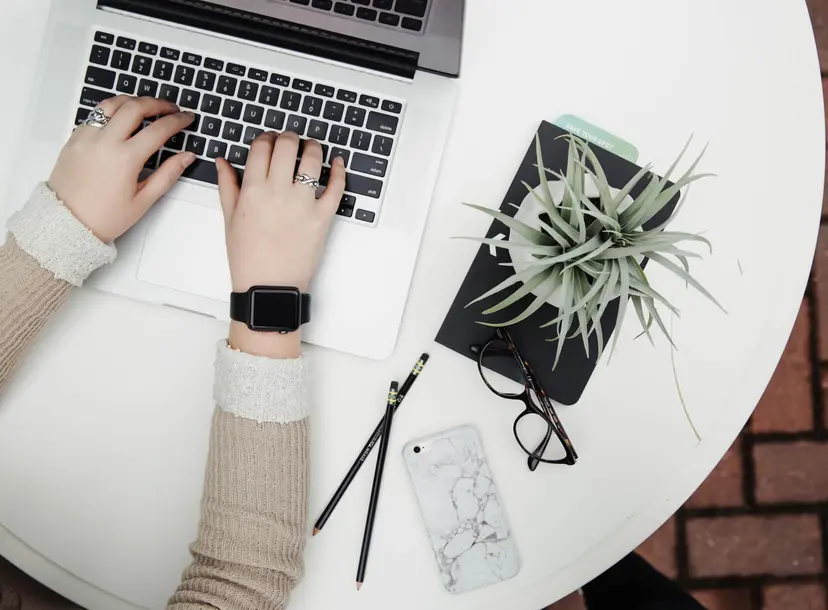 A woman's hands typing on a laptop, next to a shrub