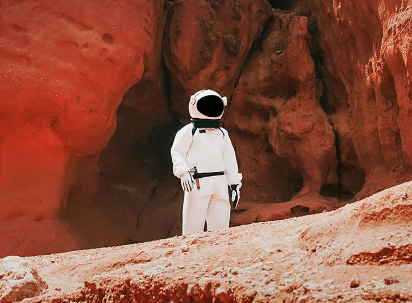 A person in a spacesuit among some red rocks