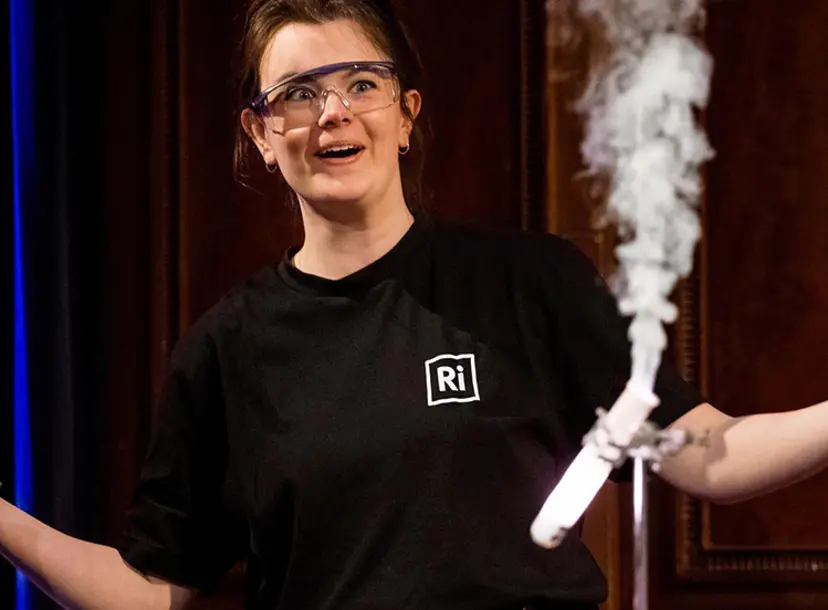 A demonstration with lots of smoke. Behind it, a woman stands with her arms open, smiling.