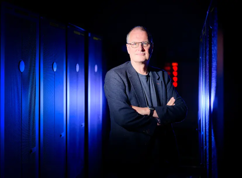 Professor Mike Wooldridge looks into the camera with a blue lit background behind him