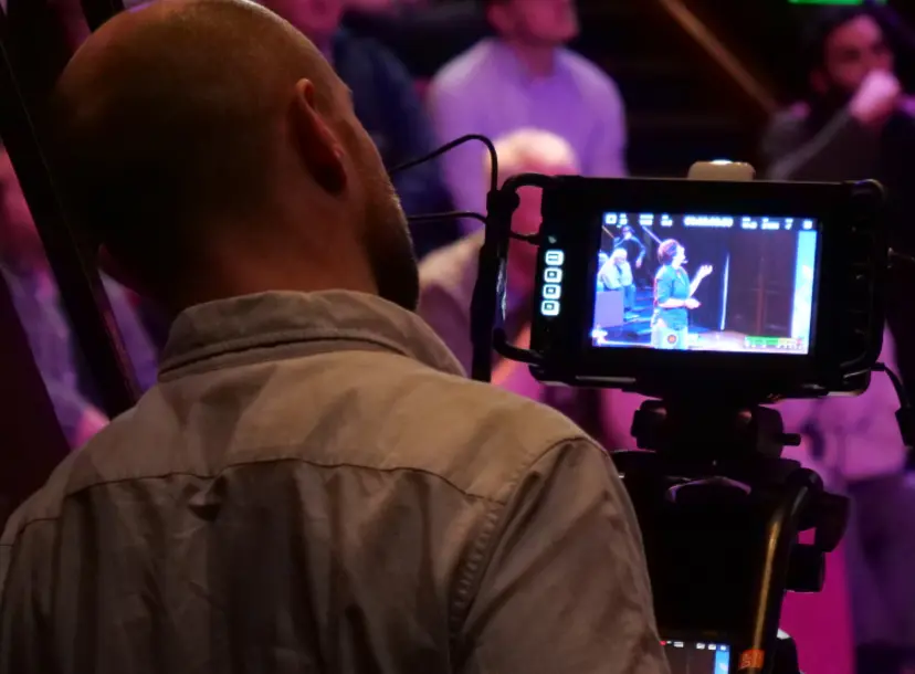 A man looks through a camera screen at the audience at an Ri talk