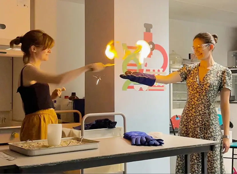 Two women taking part in a science demonstration involving fire, in a lab