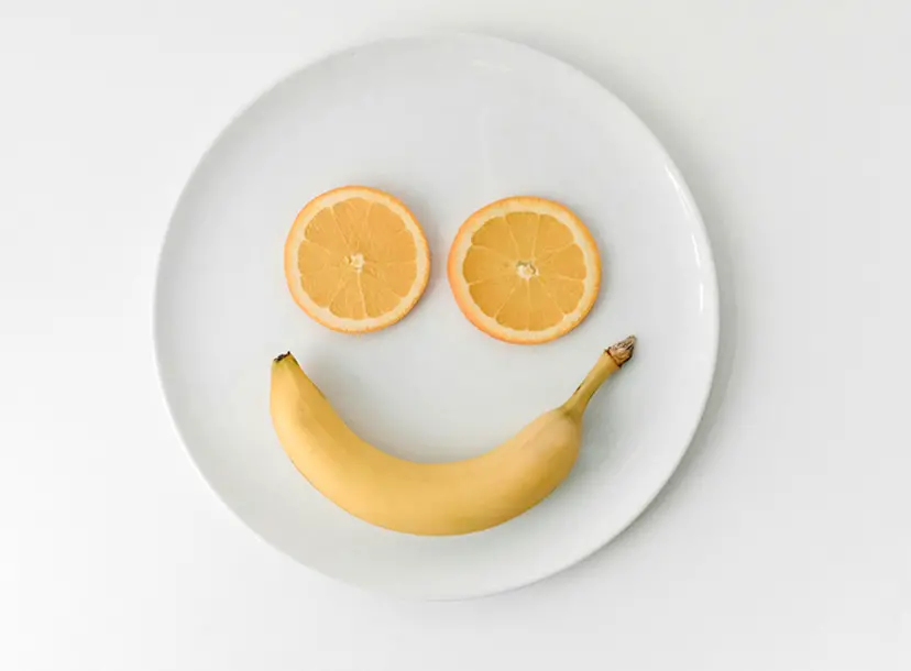 Two orange slices and a banana on a plate, making a smiley face shape