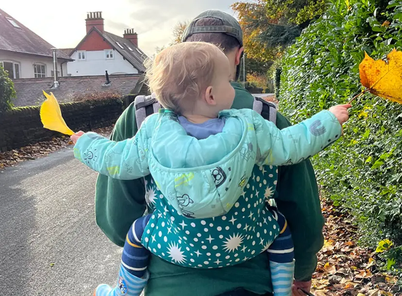 A child with curly blonde hair being carried on an adult's back with a baby backpack