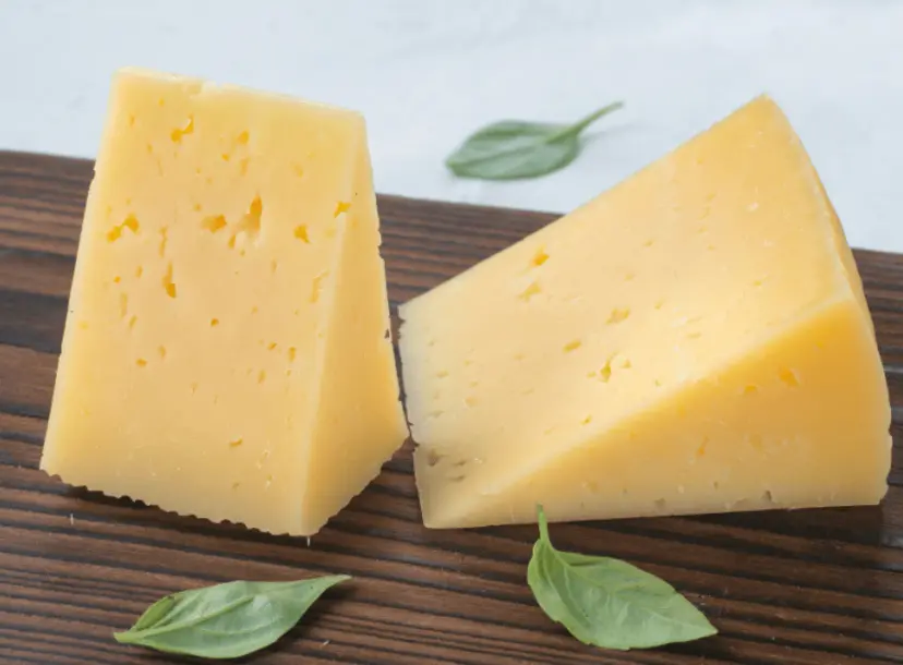 Two pieces of cheese on top of a wooden cutting board.
