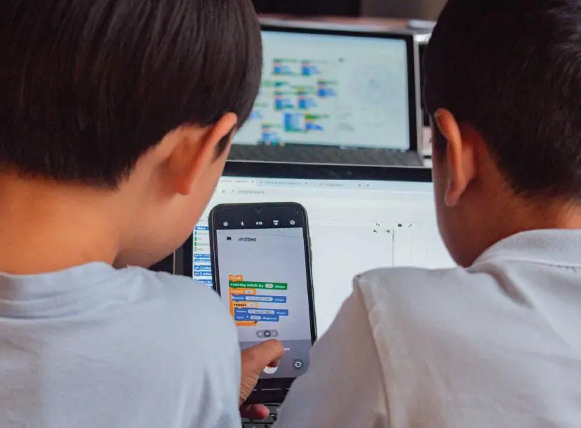 Two children stare at a screen with lines of code