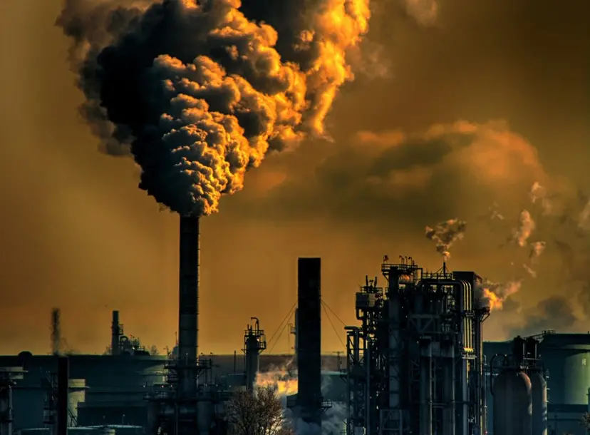 There is a landscape of chimney towers with lots of smoke coming out of them. The picture is a brown and yellow colour to show air pollution. 