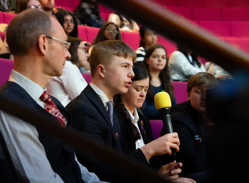 A student speaking into a microphone in a theatre setting