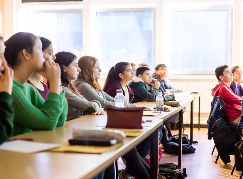 Children are sat at desks listening to a speaker