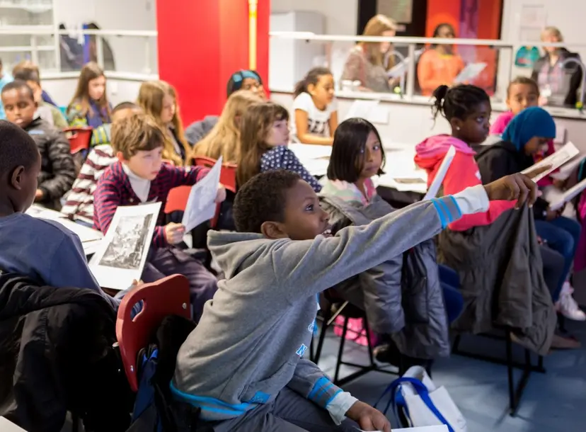 Room of enthusiastic children with their hands up at a workshop