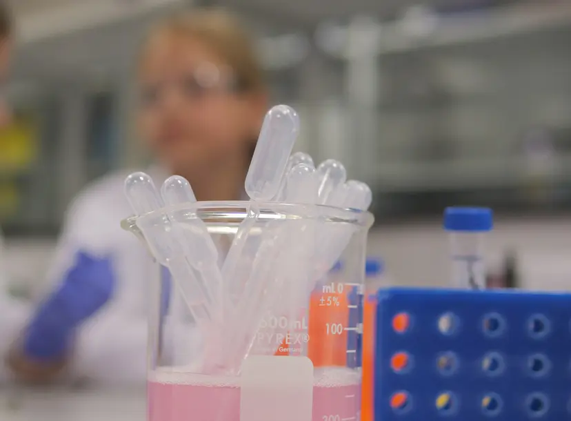 A close up of some pipettes and a test rube holder. In the background a child in a lab coat