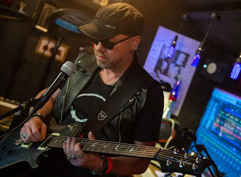 Physicist and musican Bob Coecke wearing a baseball cap holding a guitar in front of a microphone