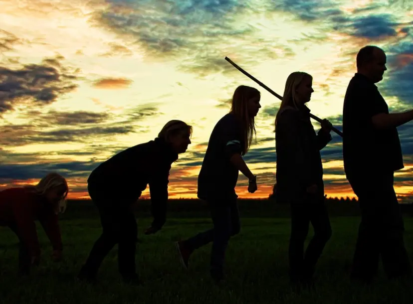 black profiles of human like structures against a sunset