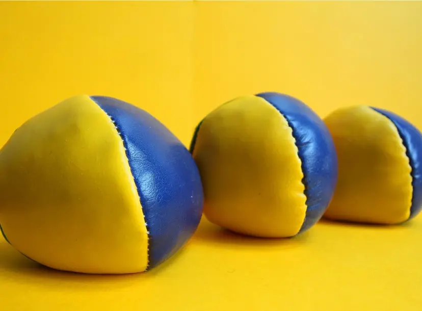 three yellow and blue juggling balls sit on a yellow surface, against a yellow background. 