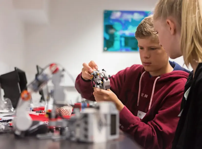 Two students, with one on the left handling part of a robot
