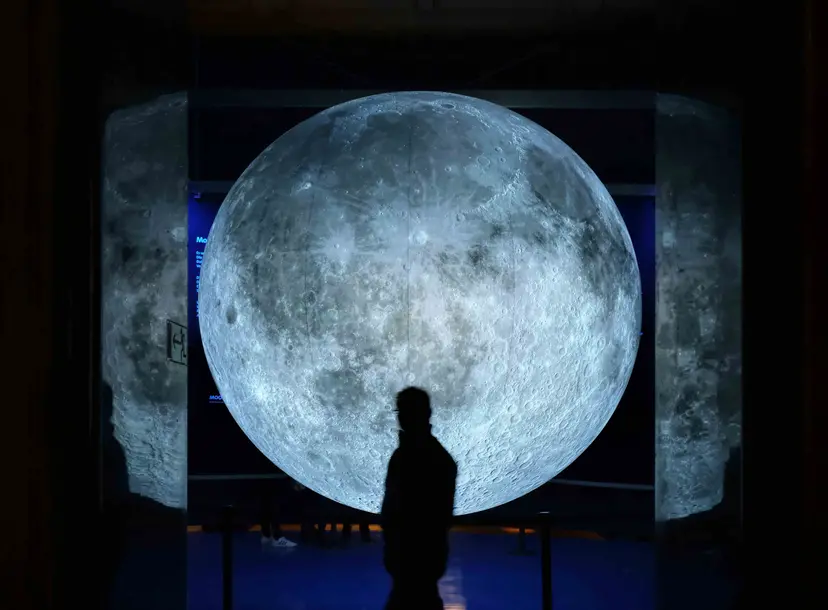 A man walks across a large picture of the moon