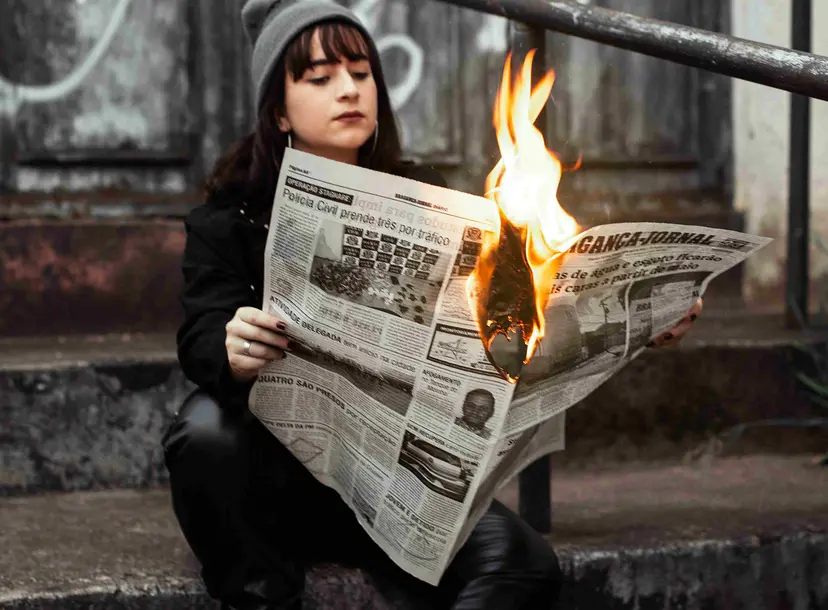 A girls reads a newspaper that is on fire in her hands