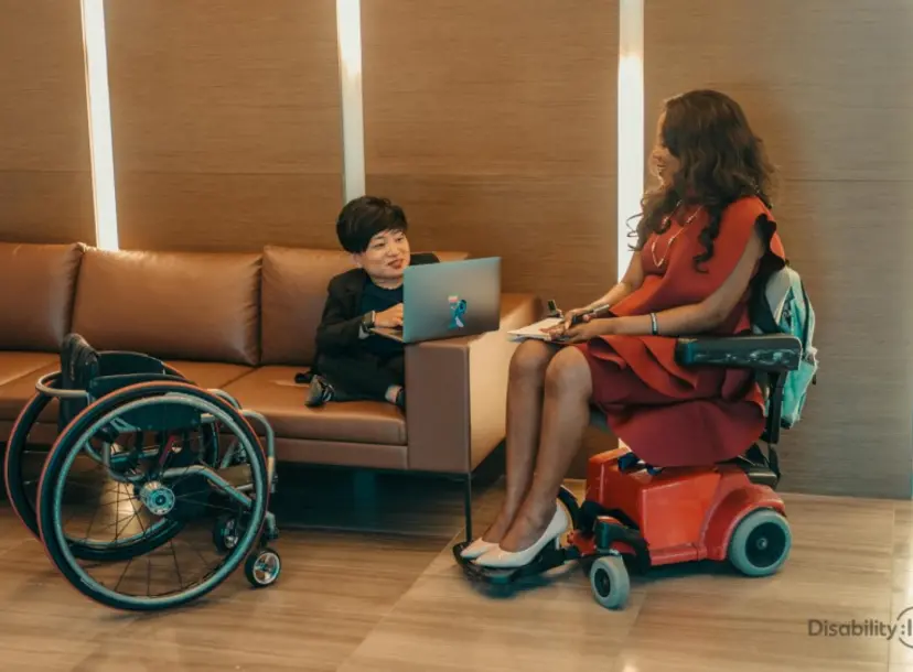 A woman is seated on a sofa, facing another woman sitting in a wheelchair. 