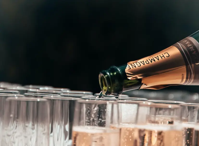 An open bottle of champagne is pouring champagne into lots of flute glasses.