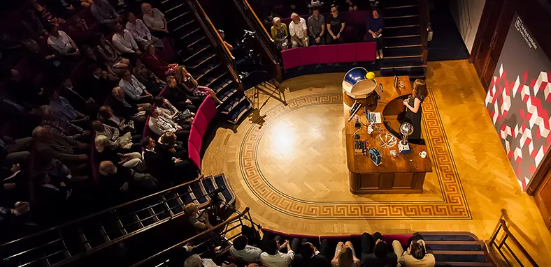 Ri lecture theatre from above, a person is presenting a talk on stage, the audience watches