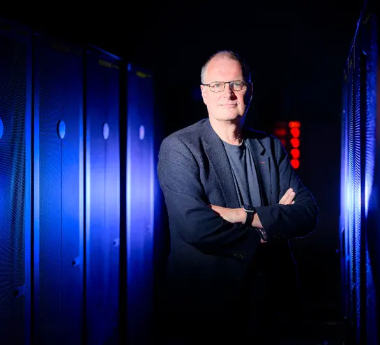 Professor Mike Wooldridge looks into the camera with a blue lit background behind him