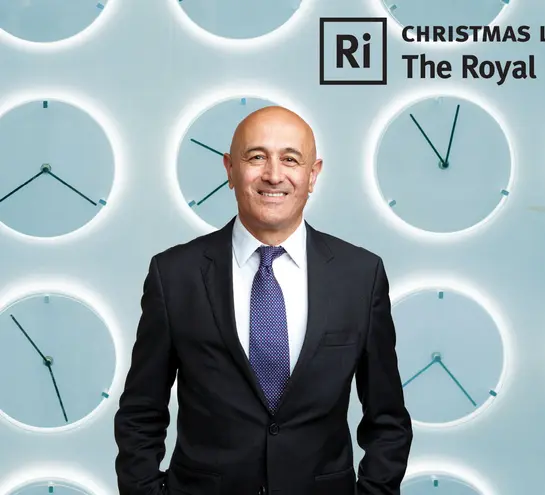 Jim Al-Khalili in front of a teal wall of analogue clocks