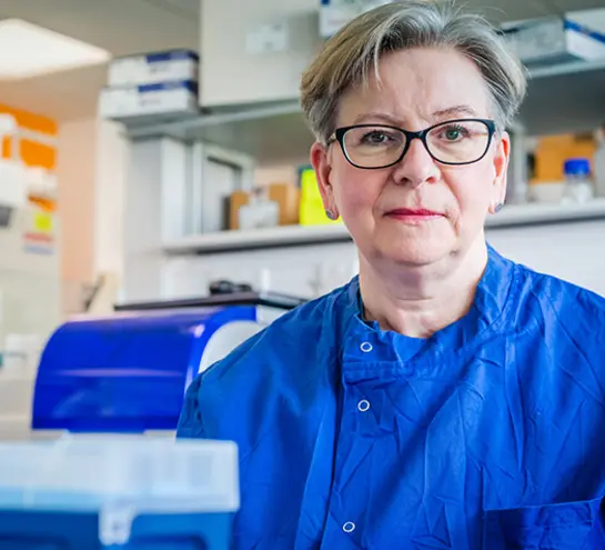 Sharon Peacock in a dark blue lab coat sitting behind a scientific apparatus