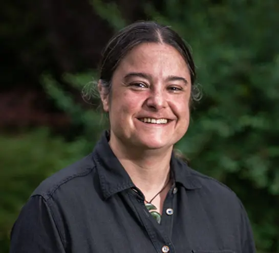 a woman with her dark hair tied back and wearing a black button up shirt and a jade spiral necklace