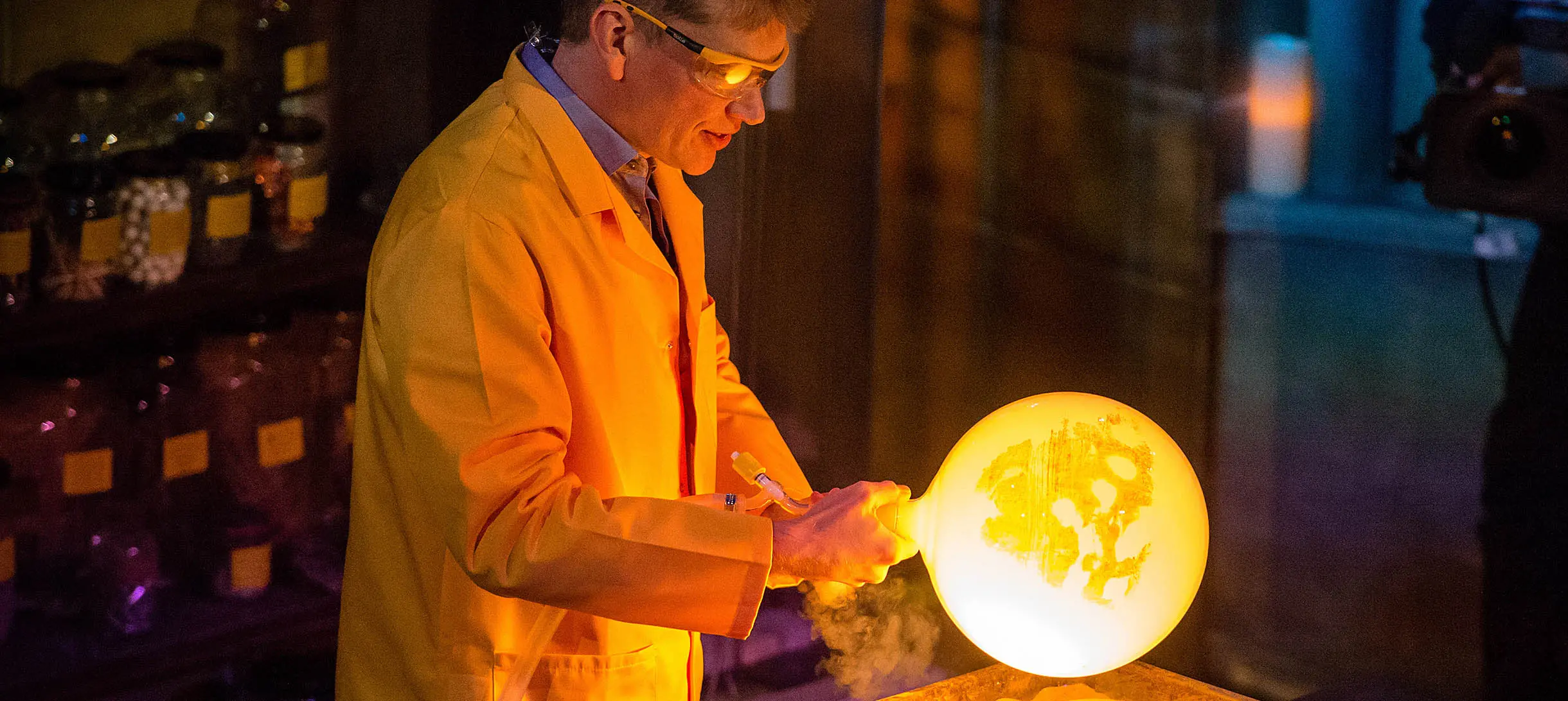 man in yellow lab coat and safety glasses is holding onto a brightly glowing yellow orb