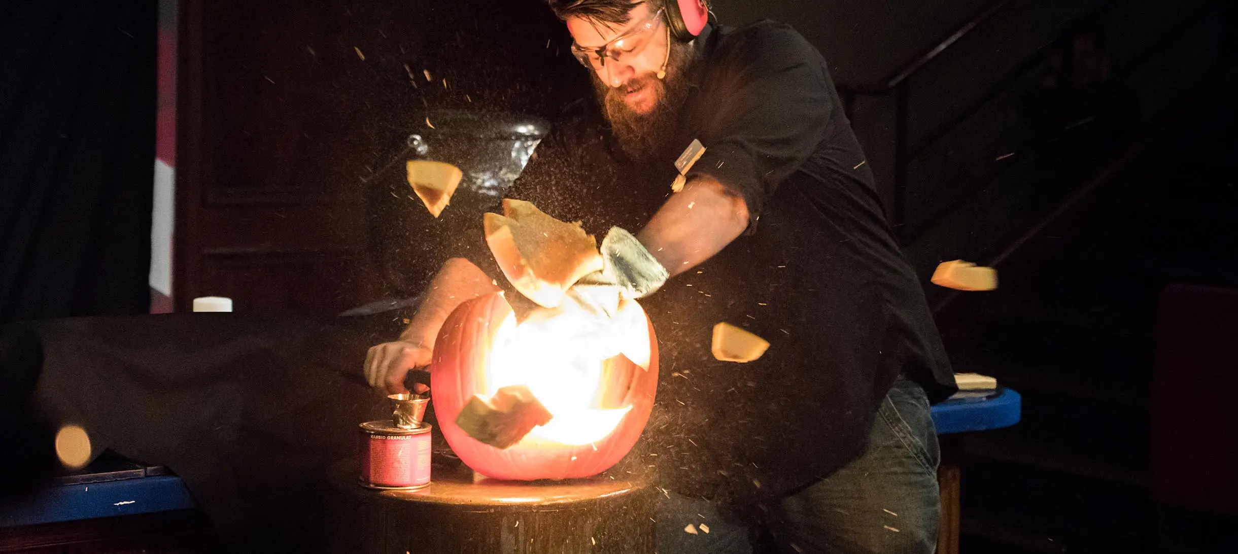 man in safety glasses and ear defenders stands behind an exploding pumpkin