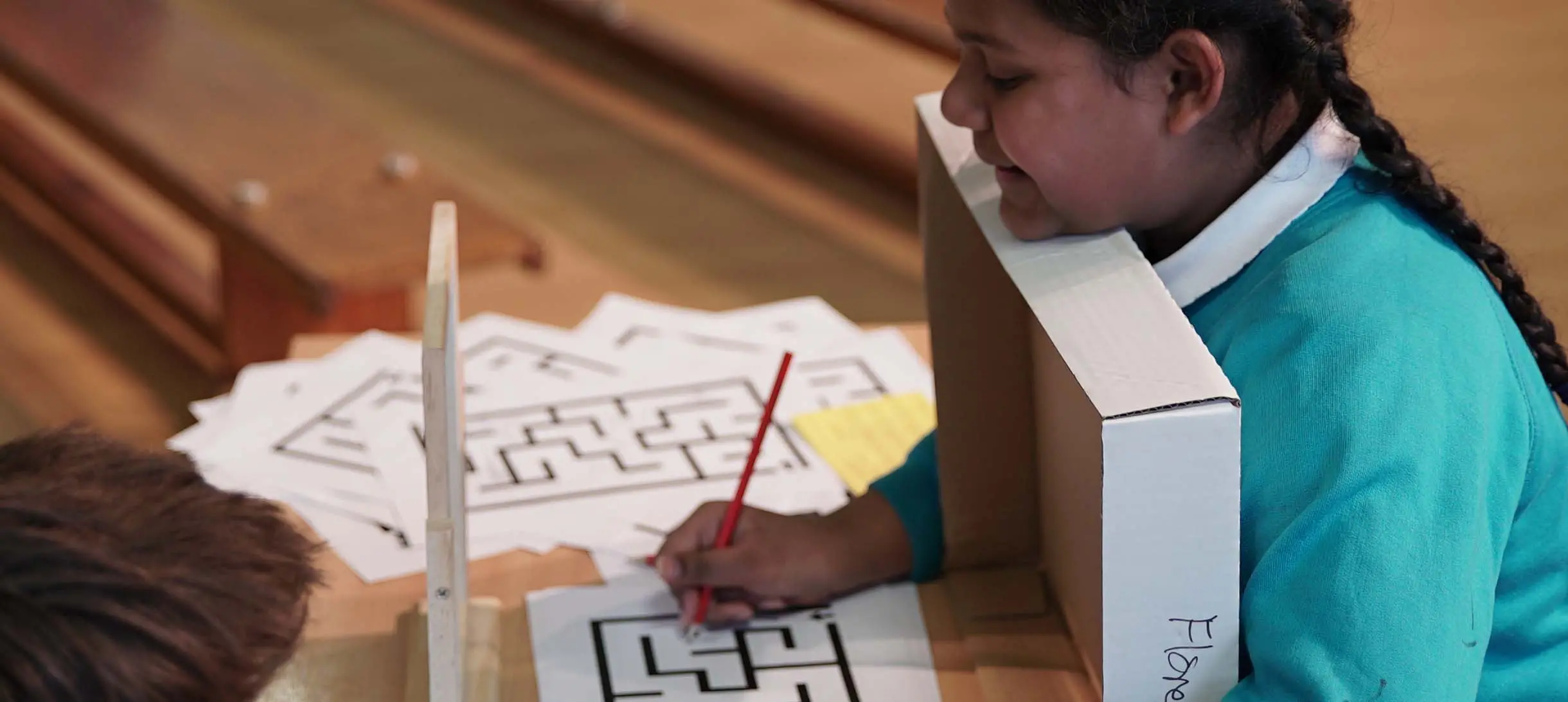 a girl in school uniform is tryin to solve a maze by looking at its reflection in the mirror