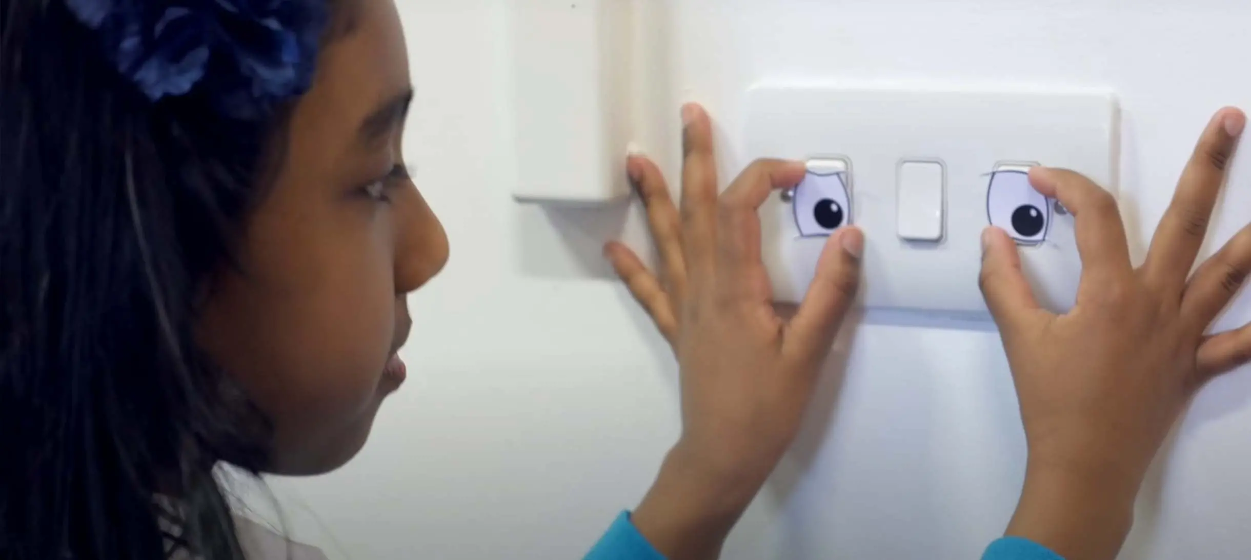 a girl is holding up two cardboard eyes over a light switch making it looks as if it's a face