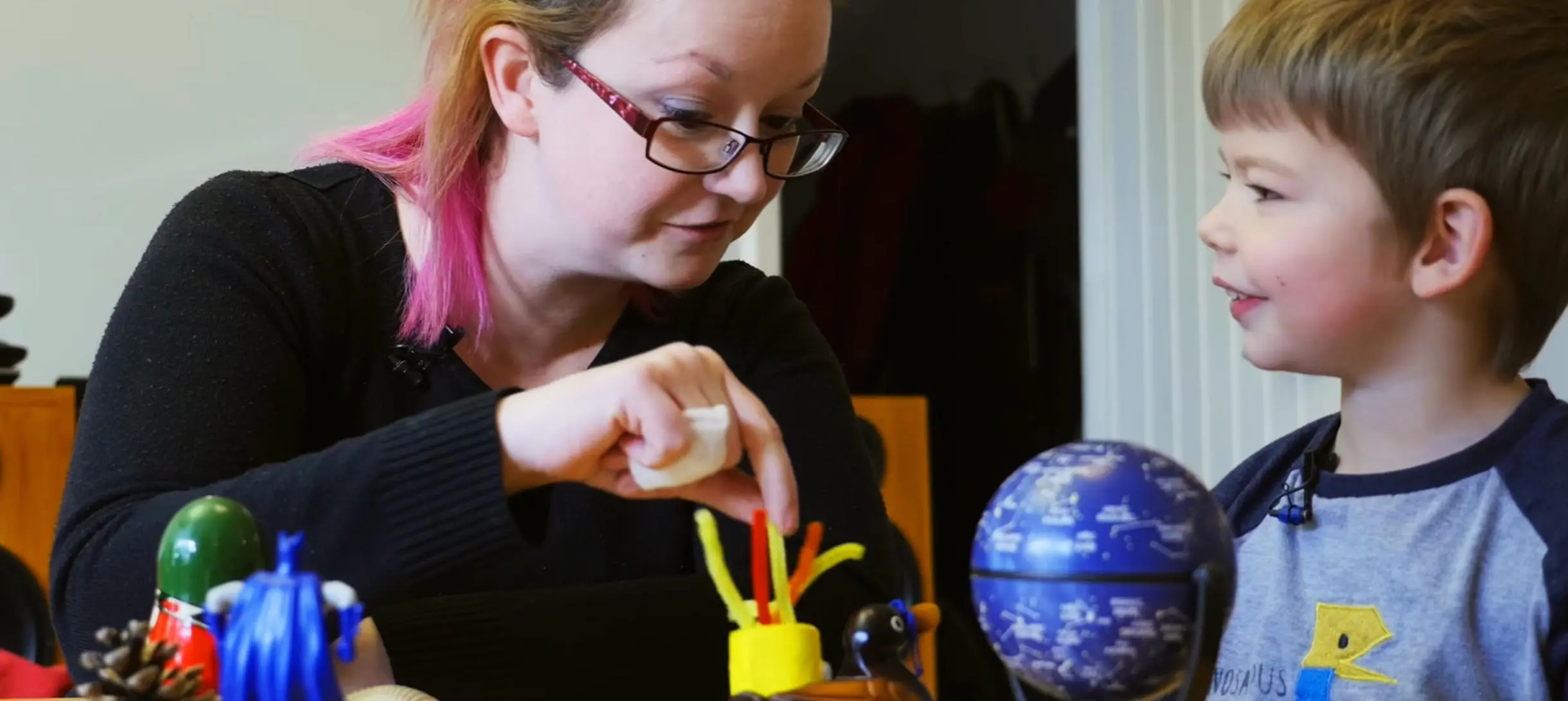 a woman and a small boy are looking at a selection of toys on the table