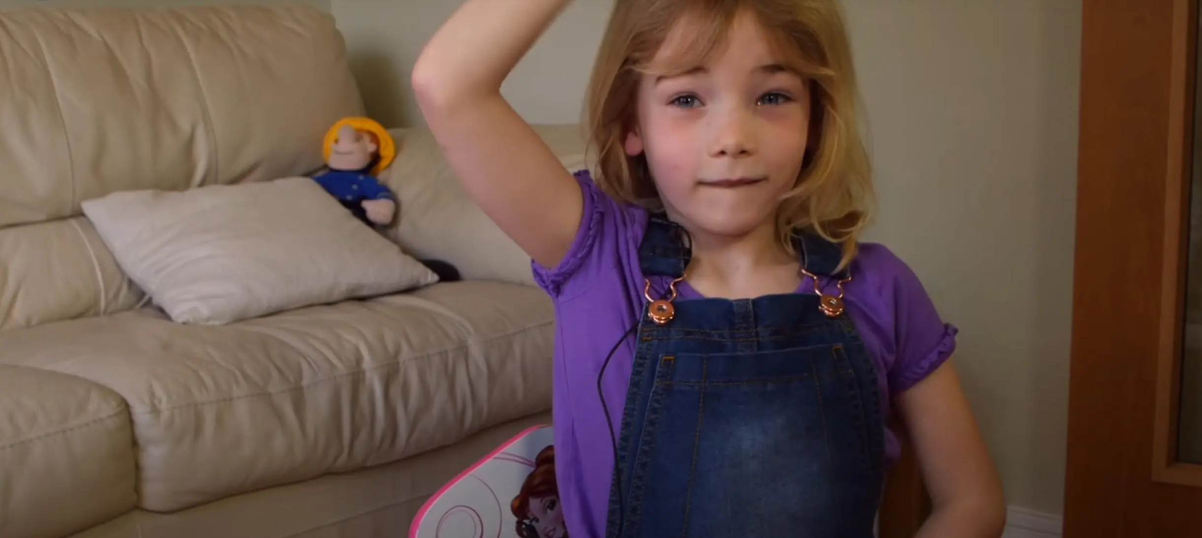 small girl in dungarees with one hand on her head and another on her belly