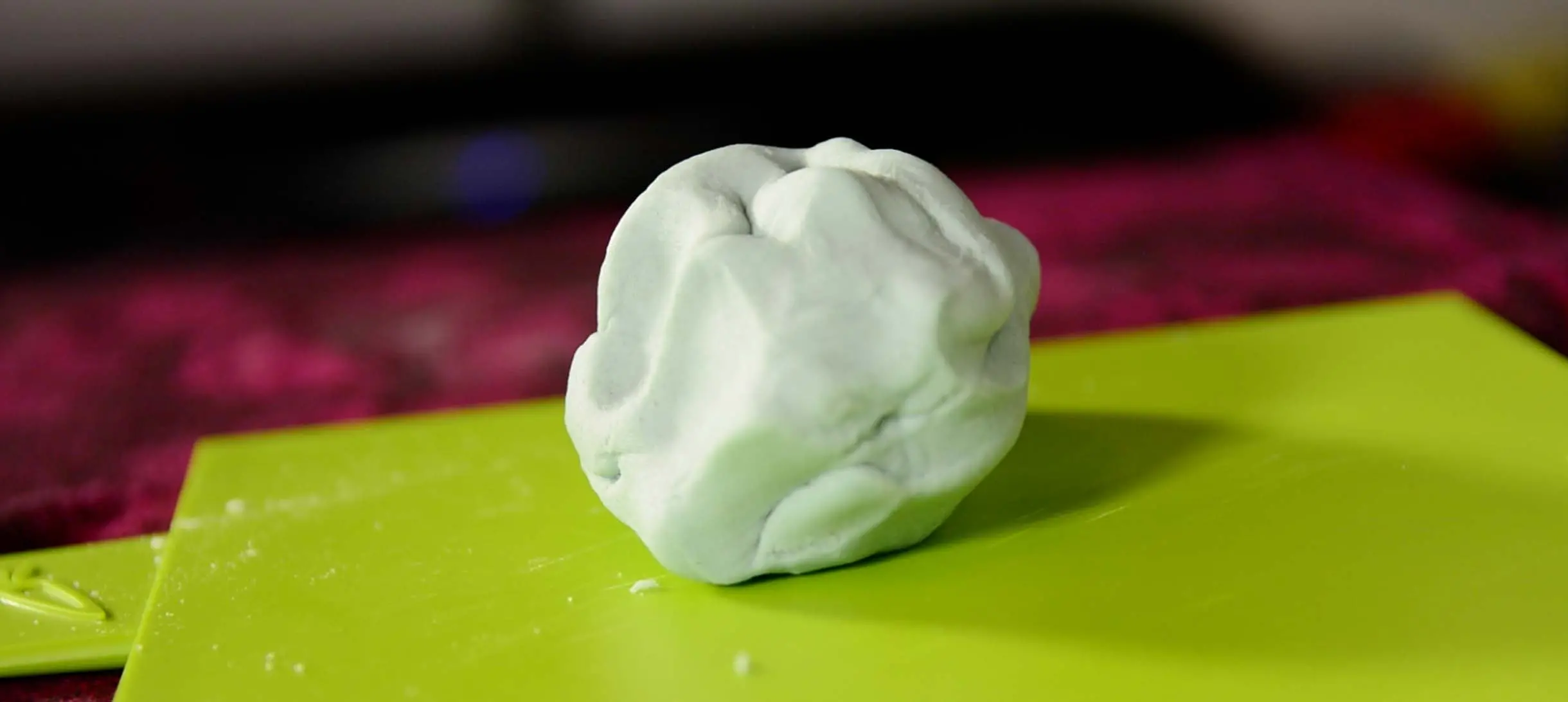 a faintly blue coloured dough ball on a bright green chopping board
