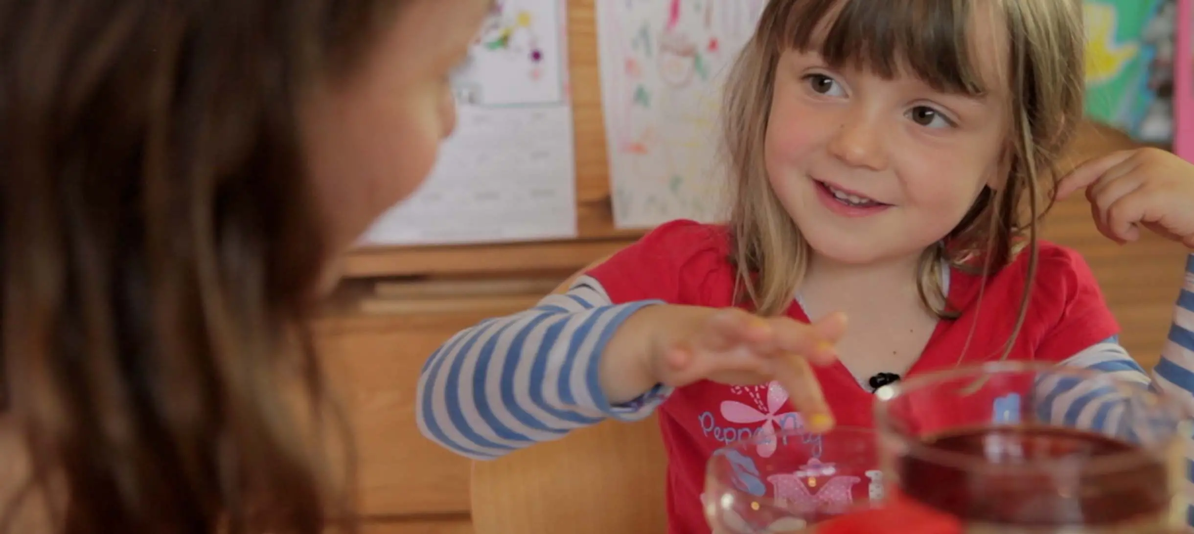 a young girl is running her finger over the rim of a glass while smiling at her mother