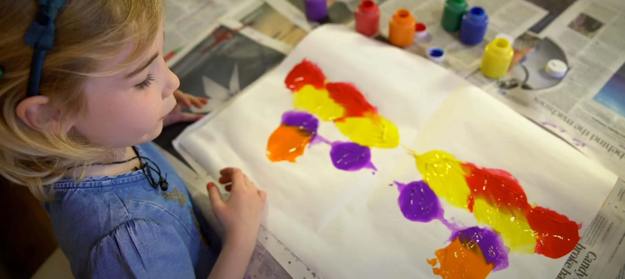 a young girl is looking at a paper covered in paint splatters