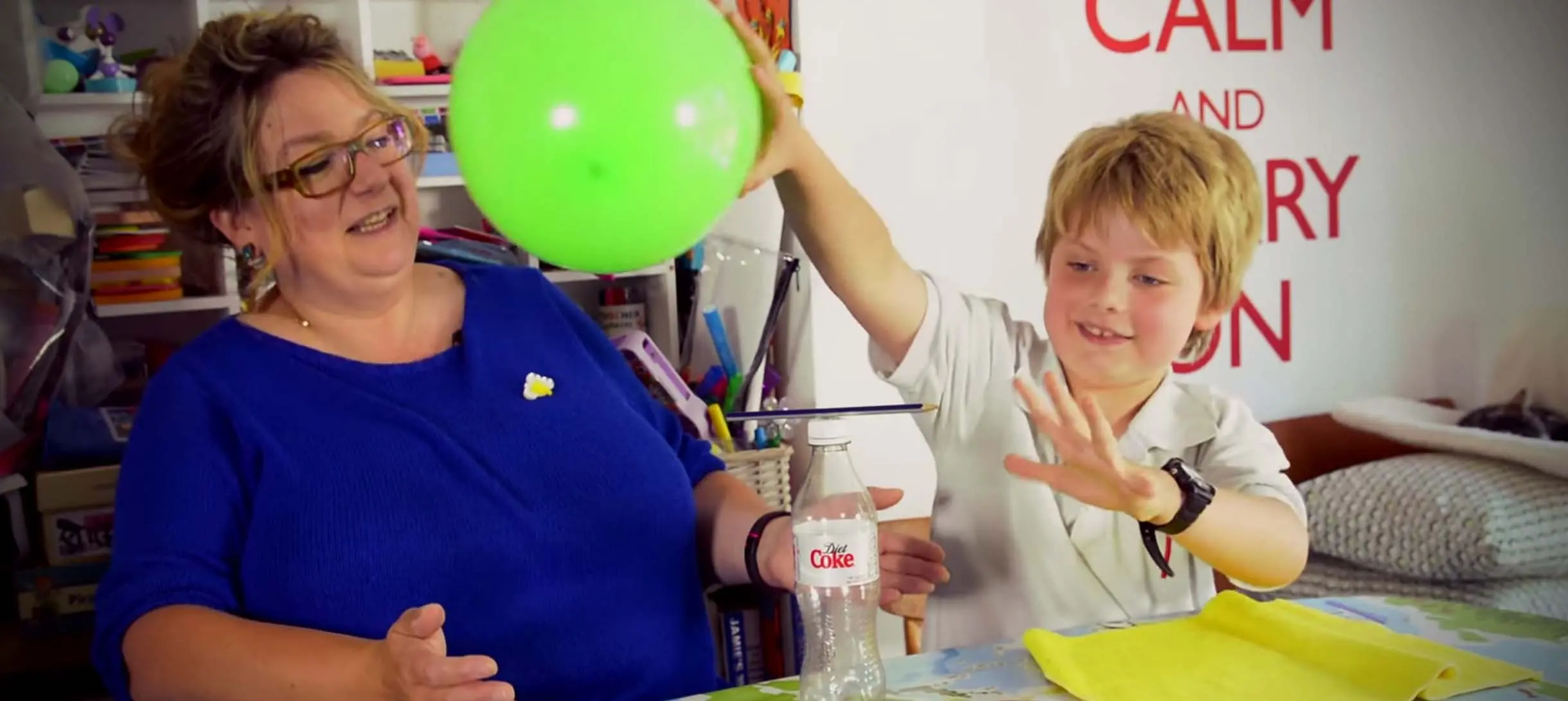 a woman with glasses leans away as a young boy holds up a balloon in one hand