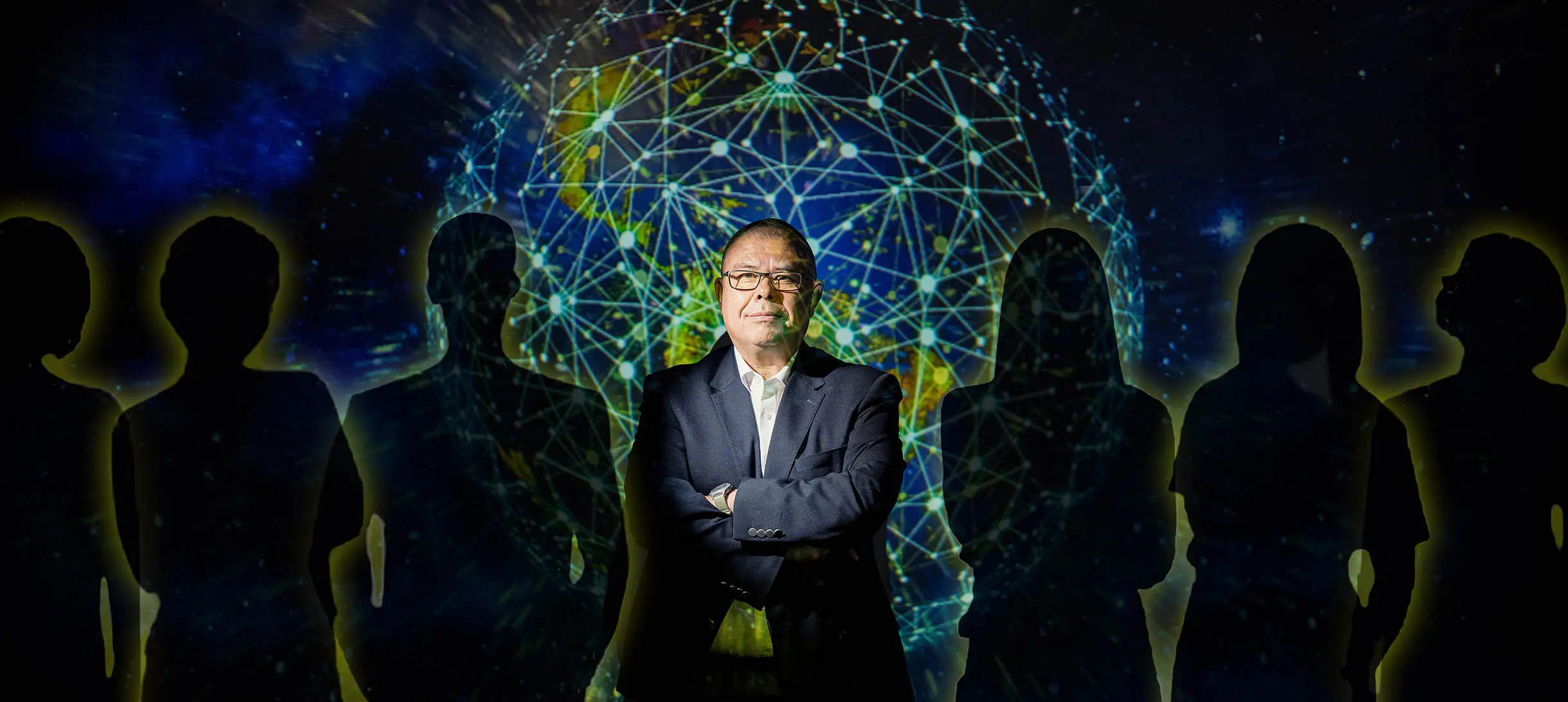 Jonathan van Tam with his arms crossed and a projection of a globe overlaying him, he's surrounded by silhouettes of six people