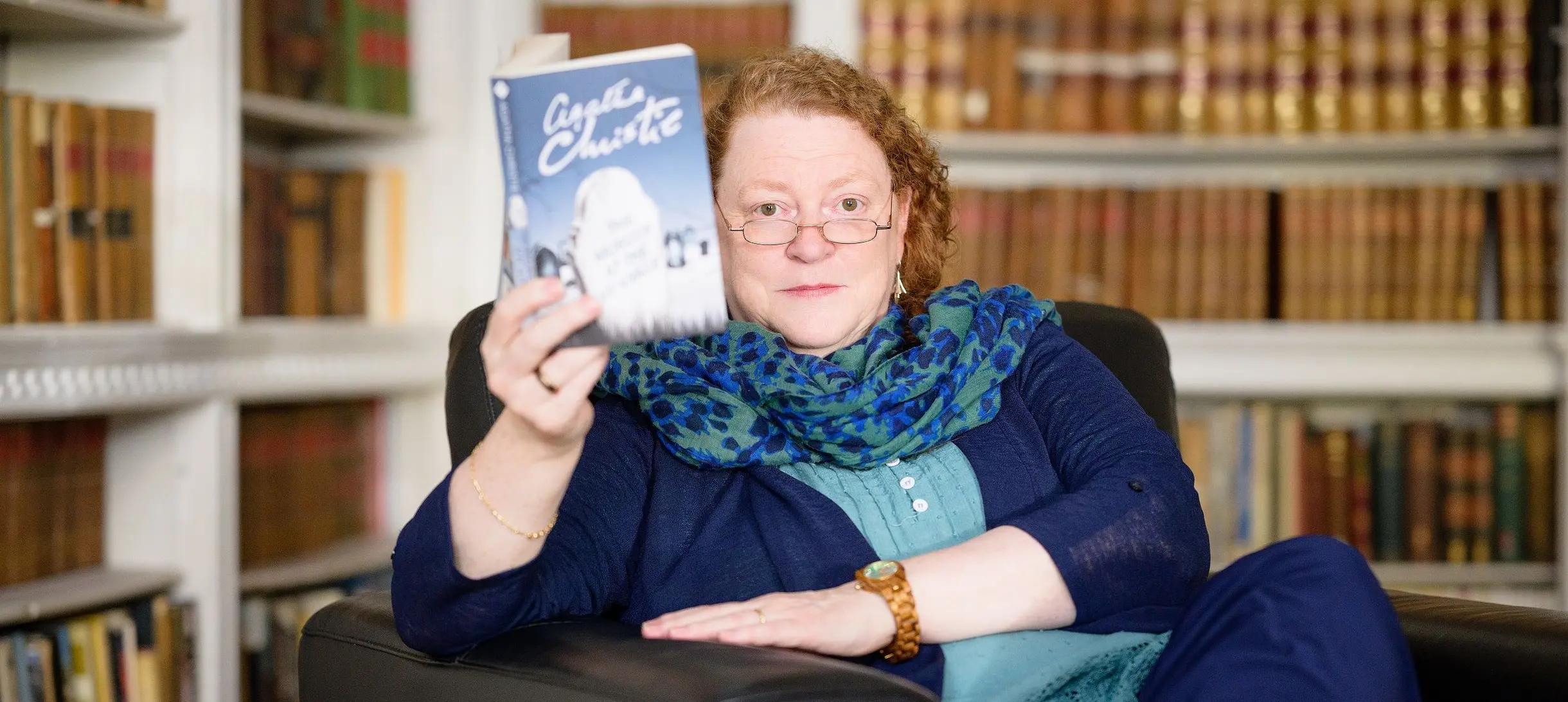Sue Black in the Ri library holding up an Agatha Christie book