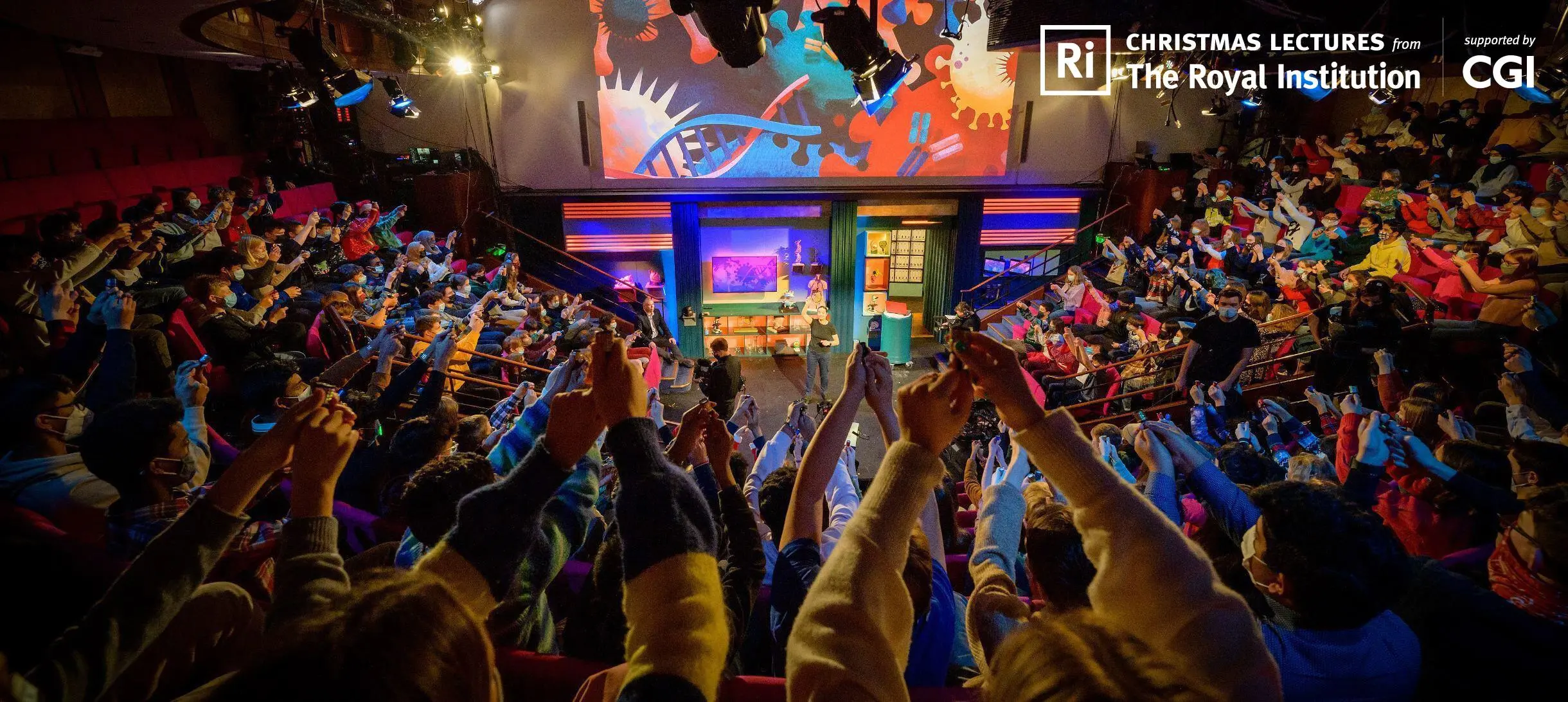Young people with their hands up during the Christmas Lectures filming in the Ri Theatre