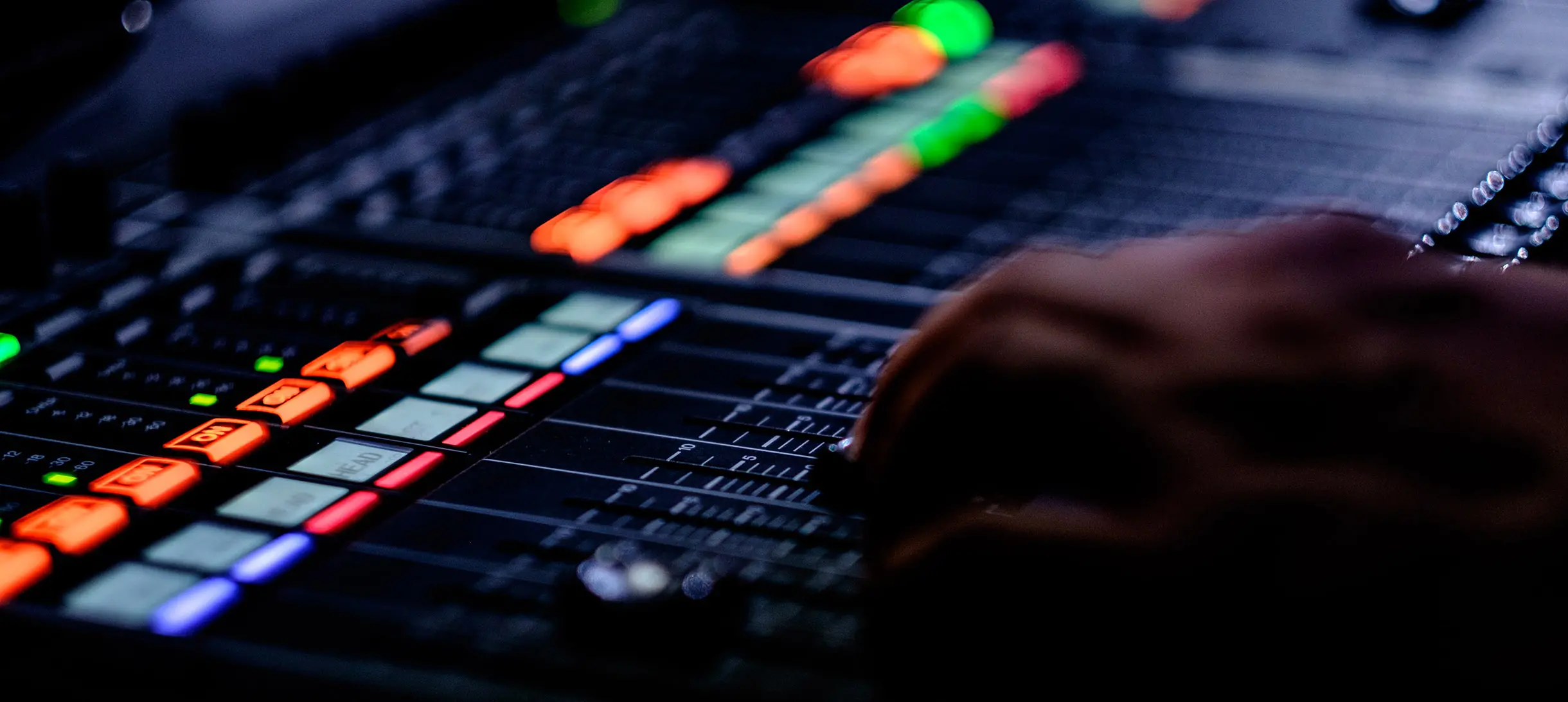 A hand operating a sound mixing machine, with lit up buttons